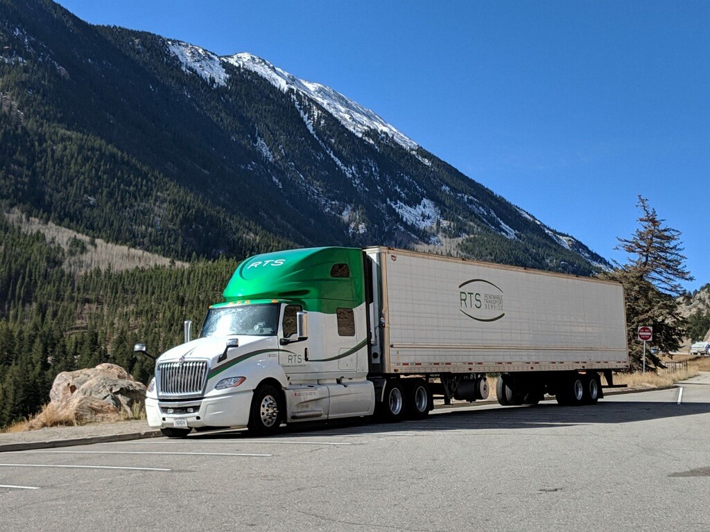 An RTS green tractor-trailer parked at a mountain overlook with snow-capped peaks